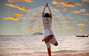 Lifestyle of young woman practicing yoga on the beach with sunset sky scene