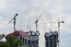 Lift tower cranes on construction site against background of the blue sky, houses new buildings near a residential area