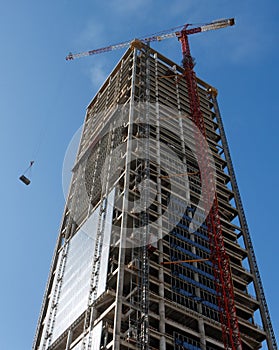 Lifting crane hoisting a weight at skyscraper cons