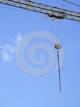A lifting hook with metal chains moves along the boom of a tower crane. Industrial background.