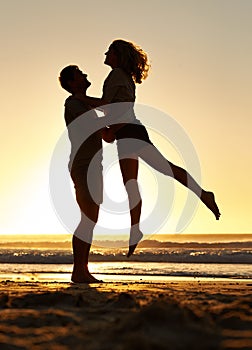 Lifting, silhouette and couple with sunset at beach, ocean and sea for affection, love and to relax. People, partners