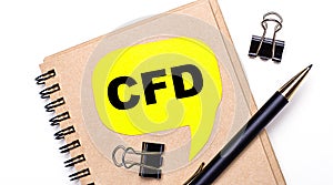 On a light background, a brown notebook, a black pen and paper clips, and a yellow card with the text CFD Contract for Difference