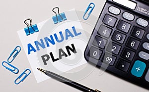 On a light background, a calculator, a pen, blue paper clips and a sheet of paper with the text ANNUAL PLAN. View from above