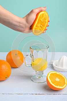 Light background, girl crushes an orange with her hand while receiving juice in a transparent glass