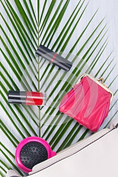 On a light background and a green leaf of a palm tree, a close-up of a white cosmetic bag and scattered objects, red nail polish,