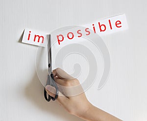 On a light background a hand holds a pair of scissors cuts a piece of paper an inscription is impossible