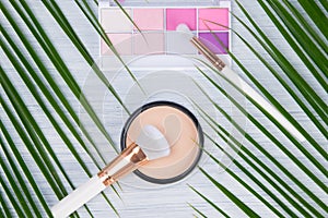 On a light background and a leaf of green palm, close-up, powder for leveling complexion with a brush and a set of multi-colored