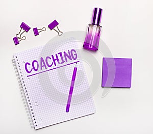 On a light background - a lilac gift, perfume, lilac business accessories and a notebook with a lilac inscription COACHING. Flat