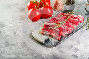 On a light background, sliced raw meat steaks on a cutting board with a sprig of rosemary, ripe tomatoes, spices, seasonings in