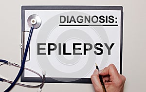 On a light background, a stethoscope and a sheet of paper, on which a man writes EPILEPSY. Medical concept