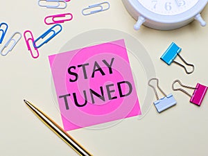 On a light background, a white alarm clock, pink, blue and white paper clips, a golden pen and a pink sticker with the text STAY