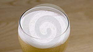 Light beer is poured into a glass on a wooden table. Freshness and foam. Slow motion. Close up.