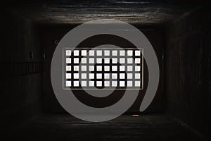 Light behind barred window in the dark prison cell - empty jail interior with grey concrete walls