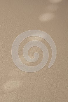Light beige toned background on a textured wall with a shadow in the form of diagonally directed blurry ovals from the window.