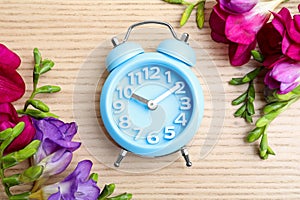 Light blue alarm clock and spring flowers on table, flat lay. Time change