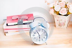 Light blue alarm clock on wooden table with books and glasses