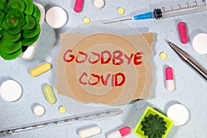 On a light blue background a card with the tex. GOODBYE CORONAVIRUS near the white bottle pills