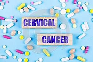 On a light blue background, multi-colored pills and wooden blocks with the text CERVICAL CANCER. Pharmaceutics. Medical concept