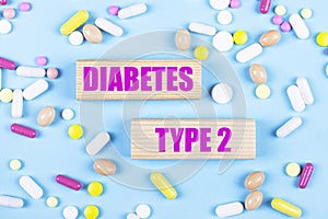 On a light blue background, multi-colored pills and wooden blocks with the text DIABETES TYPE 2. Pharmaceutics. Medical concept