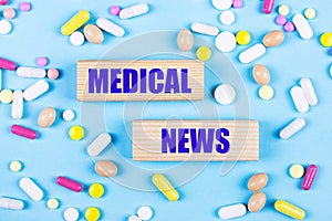 On a light blue background, multi-colored pills and wooden blocks with the text MEDICAL NEWS. Pharmaceutics. Medical concept