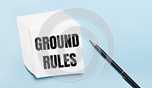 On a light blue background, there is a black pen and a stack of white note paper with the text GROUND RULES