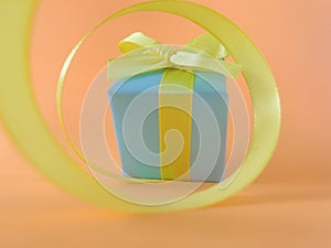 Light blue gift box at the end of the spiral yellow ribbon, orange background.