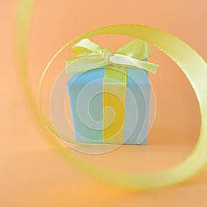 Light blue gift box at the end of the spiral yellow ribbon, orange background, square.