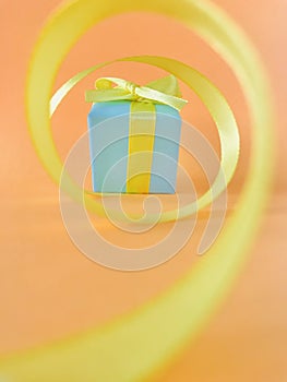 Light blue gift box at the end of the spiral yellow ribbon, orange background, vertical.
