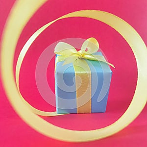 Light blue gift box at the end of the spiral yellow ribbon, red background. square.