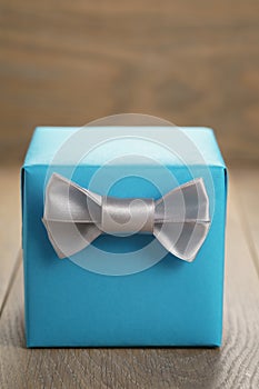 Light blue gift box with minimalistic silver ribbon bow on wooden table
