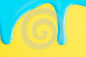 Light blue liquid drops of paint color flow down on yellow paper background. Blue paint dripping on the yellow wall with copy