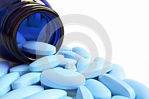 Light blue oval shaped pills scattered from deep blue glass bottle on white background