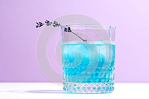 Light blue refreshing lavender alcoholic cocktail with lavender sprig on lilac background