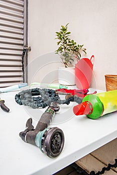 A light blue smooth metal table filled with gardening objects next to a pot of ficus benjamina and a diffuser head from a hose in