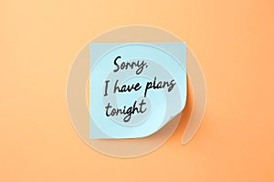 Light blue sticky note with phrase Sorry, I Have Plans Tonight on pale orange background