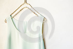 Light blue tank top hanging on a hanger in a white wall. Close up