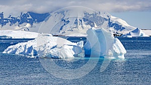 Light Blue and Turquoise Textured Iceberg in Front of Mountain Chain and Glacier in Antarctica