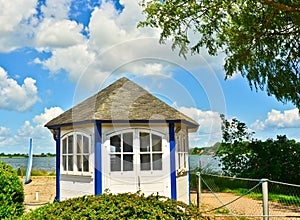 A light blue and white wooden small shed, pavilion, hexagonal at the waterside in summer