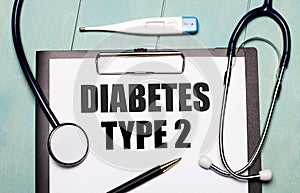 On a light blue wooden background, there is a paper labeled DIABETES TYPE 2, a stethoscope, an electronic thermometer, and a pen.