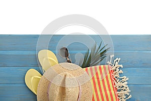 Light blue wooden surface with beach towel, straw hat, flip flops and sunglasses on white background, top view