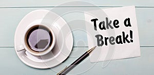 On a light blue wooden tray, there is a white cup of coffee, a handle and a napkin that says TAKE A BREAK