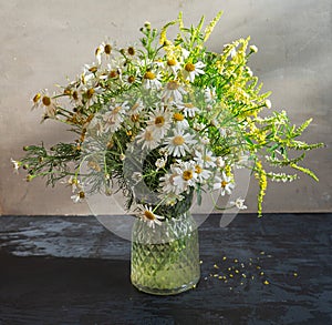 Light bouquet of wildflowers with the prevalence of daisies in a glass vase on a dark table photo