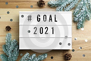 Light box with hashtag Goal 2021 near fir branches and cones on wooden table, flat lay. New year targets