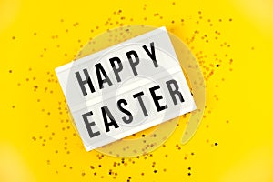 Light box over bright yellow background with the text Happy Easter. Easter celebration concept. Golden eggs and stars