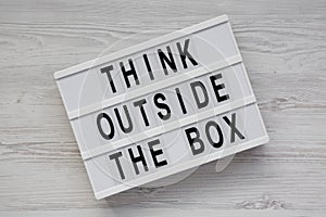 Light box with `Think outside the box` words on a white wooden surface, top view. Flat lay, overhead, from above. Close-up