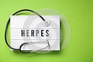 Light box with word Herpes and stethoscope on green background, top view. Space for text