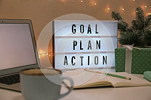 Light box with words Goal, Plan, Action near laptop and gift on table