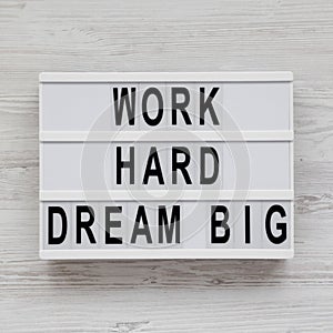 Light box with `Work hard dream big` words on a white wooden background, top view. Flat lay, overhead, from above. Close-up