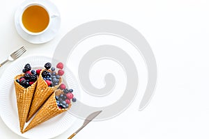 Light breakfast with fresh berries in waffle cones and cup of tea on served white table background top view mockup