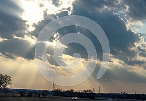 Light breaking through clouds over highway with cars at twilight with electric towers with factory in background